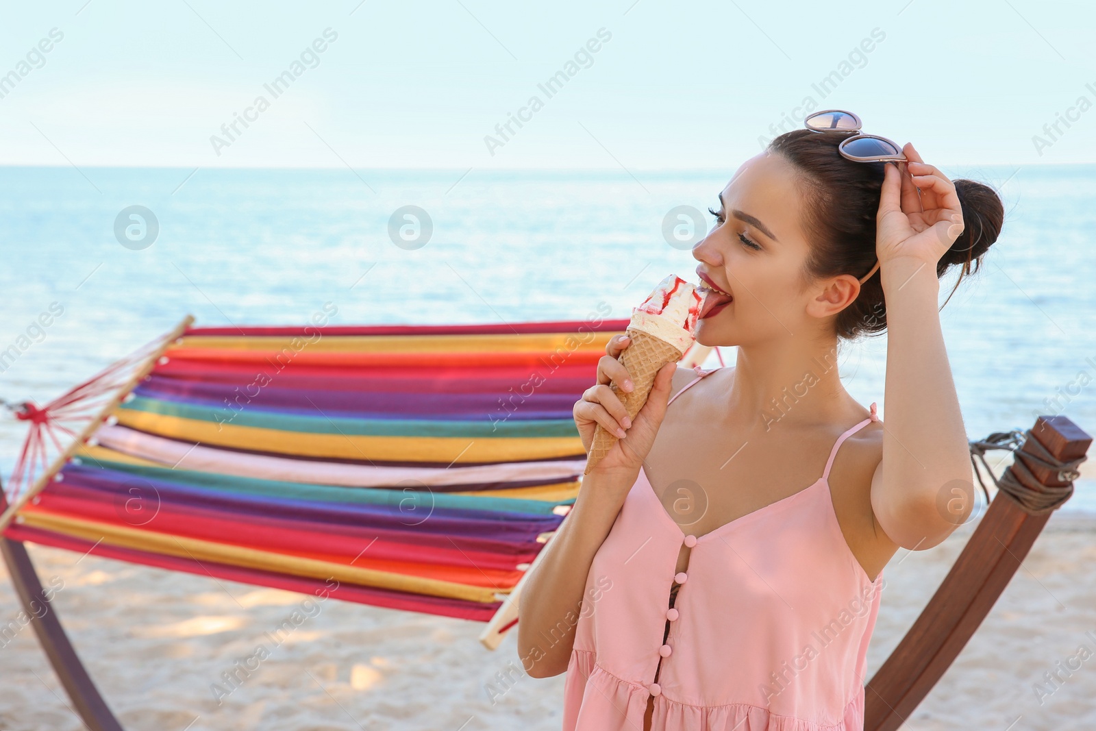 Photo of Young woman eating ice cream near hammock at seaside