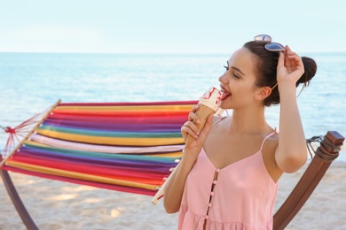 Photo of Young woman eating ice cream near hammock at seaside