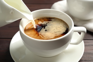 Pouring milk into cup of hot coffee on wooden table, closeup