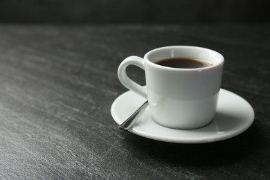 Photo of Hot coffee in cup and saucer on dark textured table, closeup. Space for text