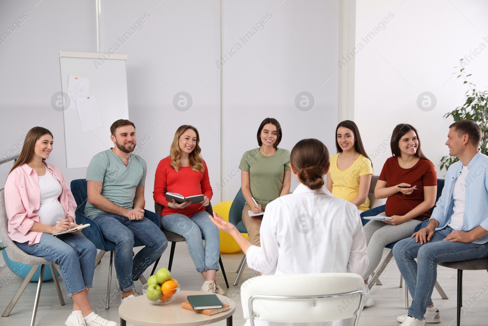 Photo of Group of pregnant women with men and doctor at courses for expectant parents indoors