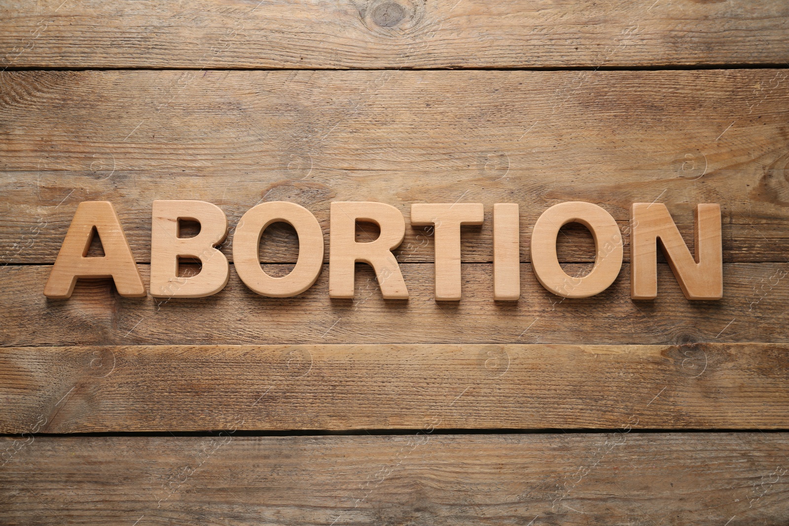 Photo of Word Abortion made of letters on wooden background, flat lay