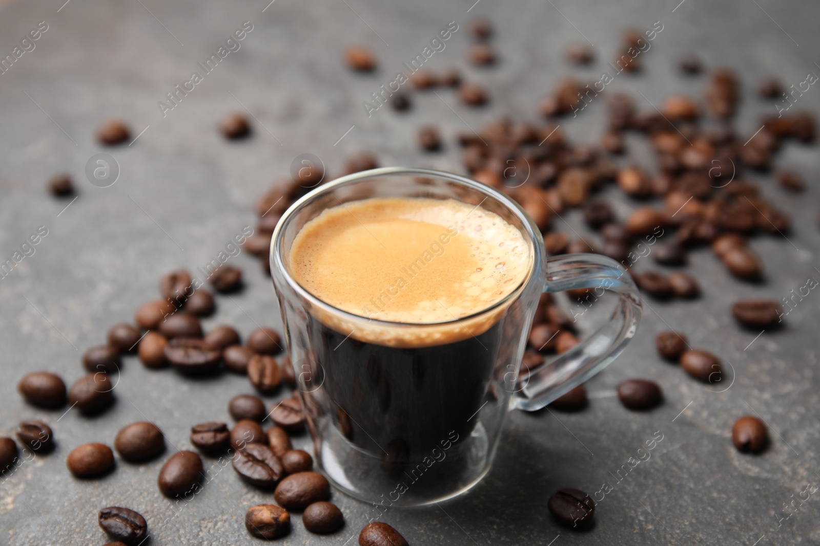 Photo of Cup of tasty espresso and scattered coffee beans on grey table