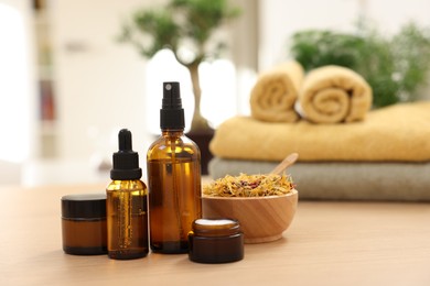 Bottles of essential oils, dry flowers and jars with cream on light wooden table, space for text. Spa therapy