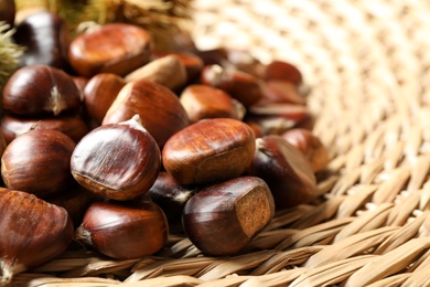 Photo of Fresh sweet edible chestnuts on wicker mat, closeup