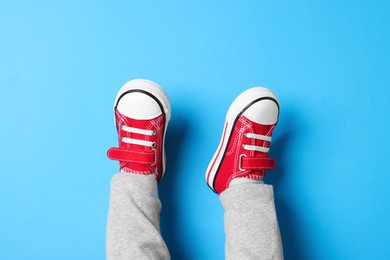 Photo of Little child in stylish red gumshoes on light blue background, top view