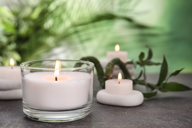 Photo of Burning candles, spa stones and bamboo sprout on grey table against blurred green background, space for text