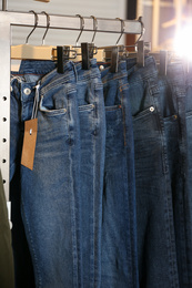 Photo of Modern jeans hanging on clothing rack in shop