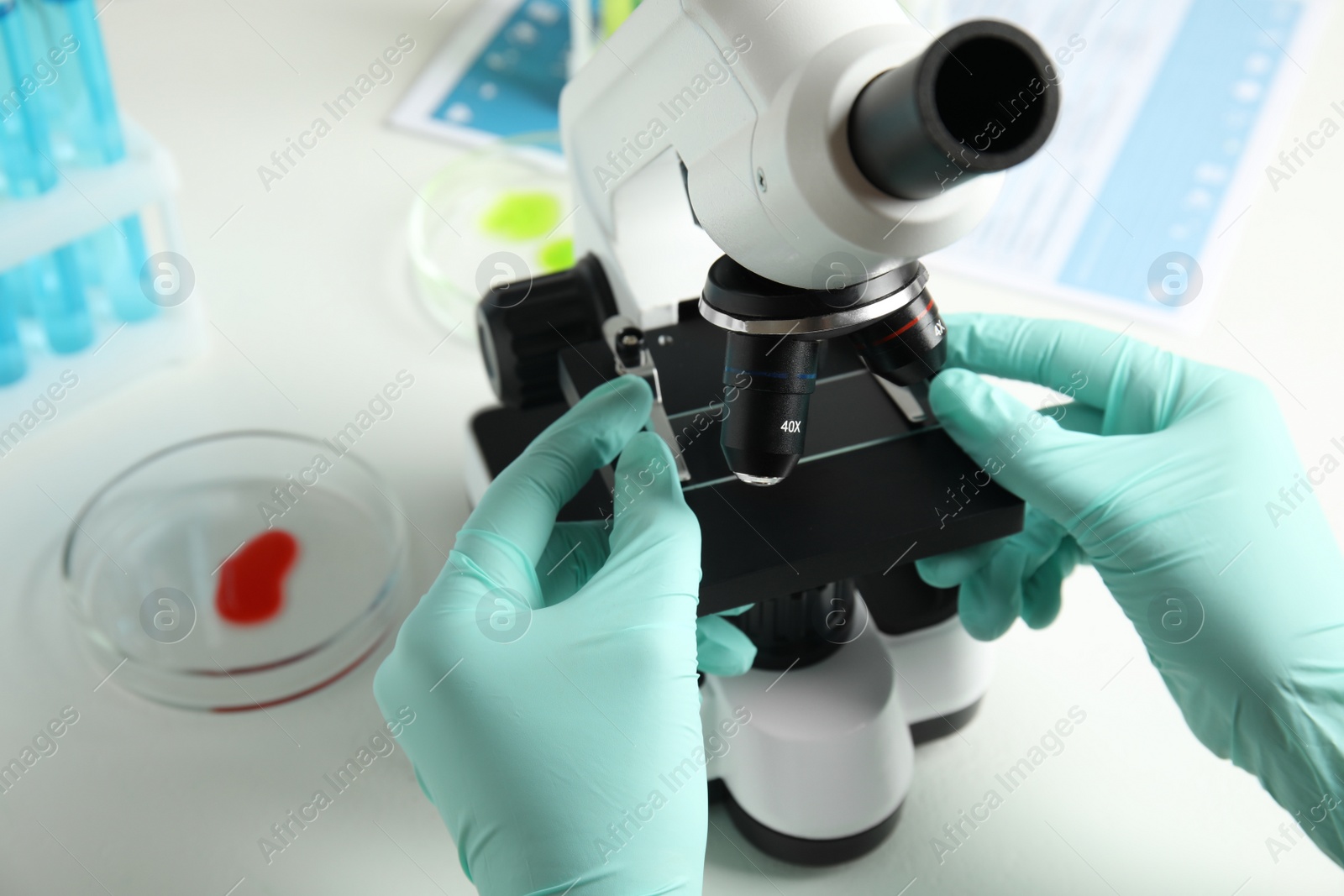 Photo of Medical assistant using modern microscope at white table, closeup