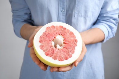 Photo of Woman holding half of red pomelo on light background, closeup