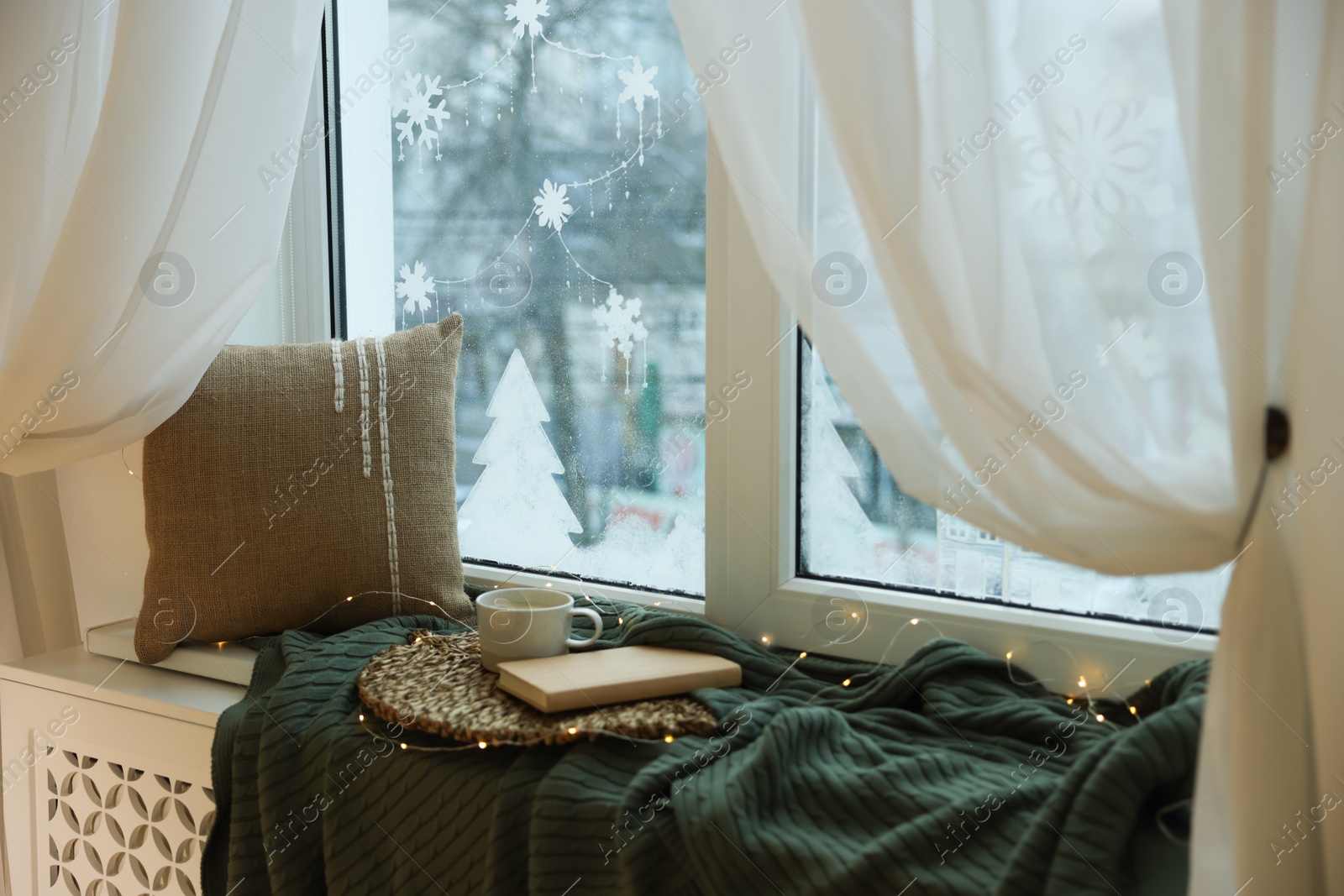 Photo of Cup of drink, book and beautiful drawing made with artificial snow on window at home. Christmas decor