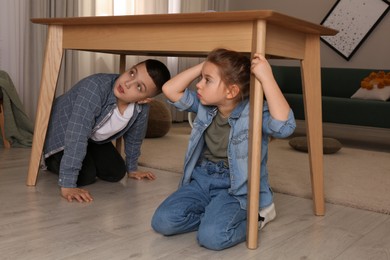 Photo of Scared children hiding under table in living room during earthquake