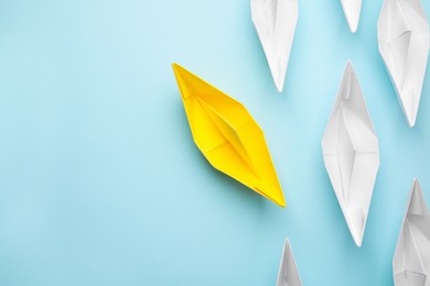 Photo of Yellow paper boat floating away from others on light blue background, flat lay with space for text. Uniqueness concept
