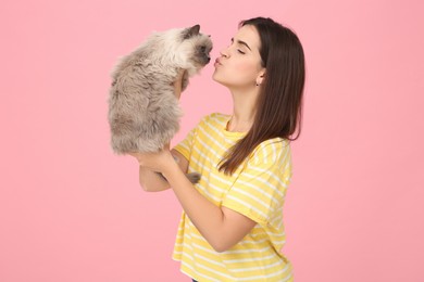 Photo of Woman kissing her cute cat on pink background