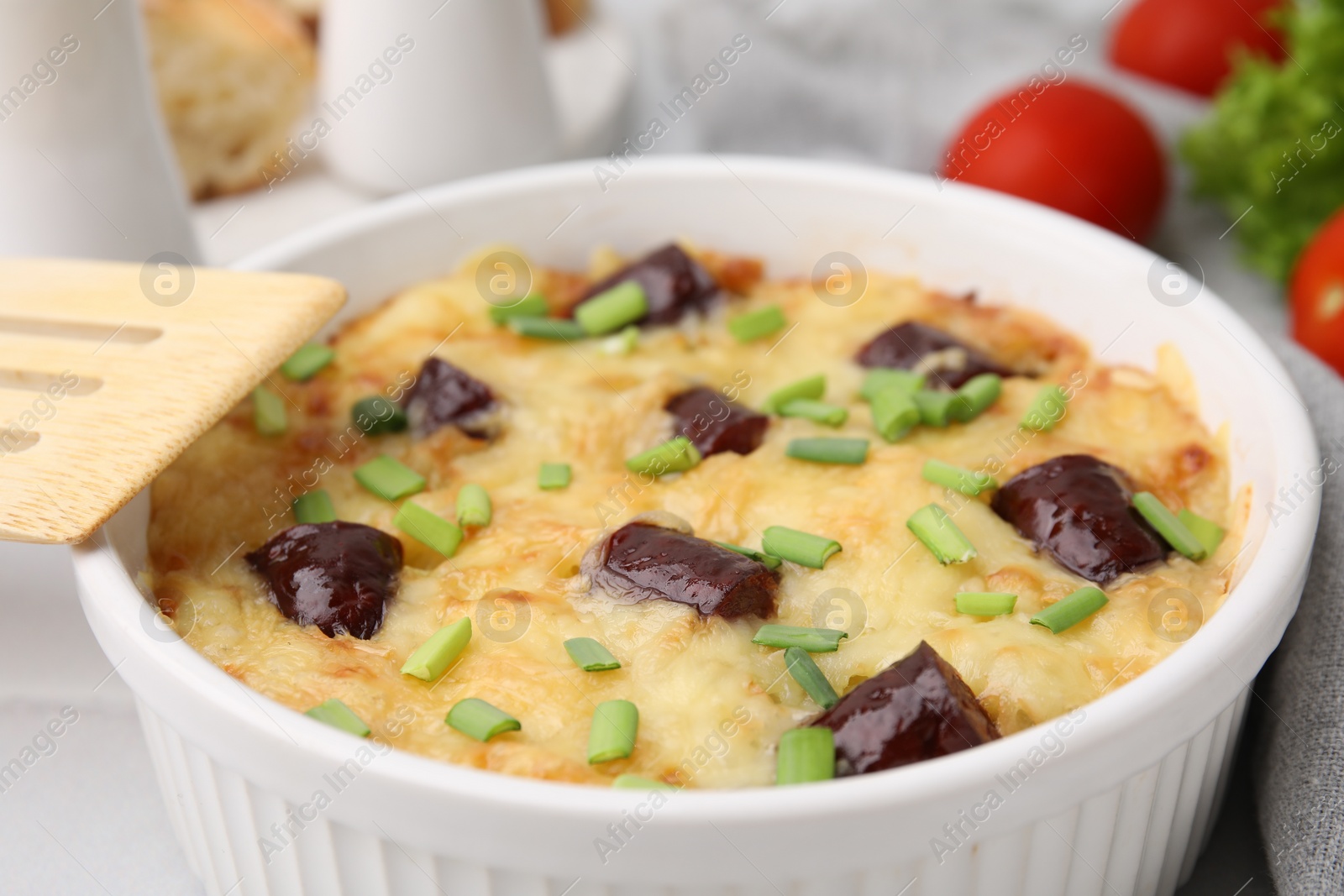 Photo of Tasty sausage casserole with green onions in baking dish served on table, closeup