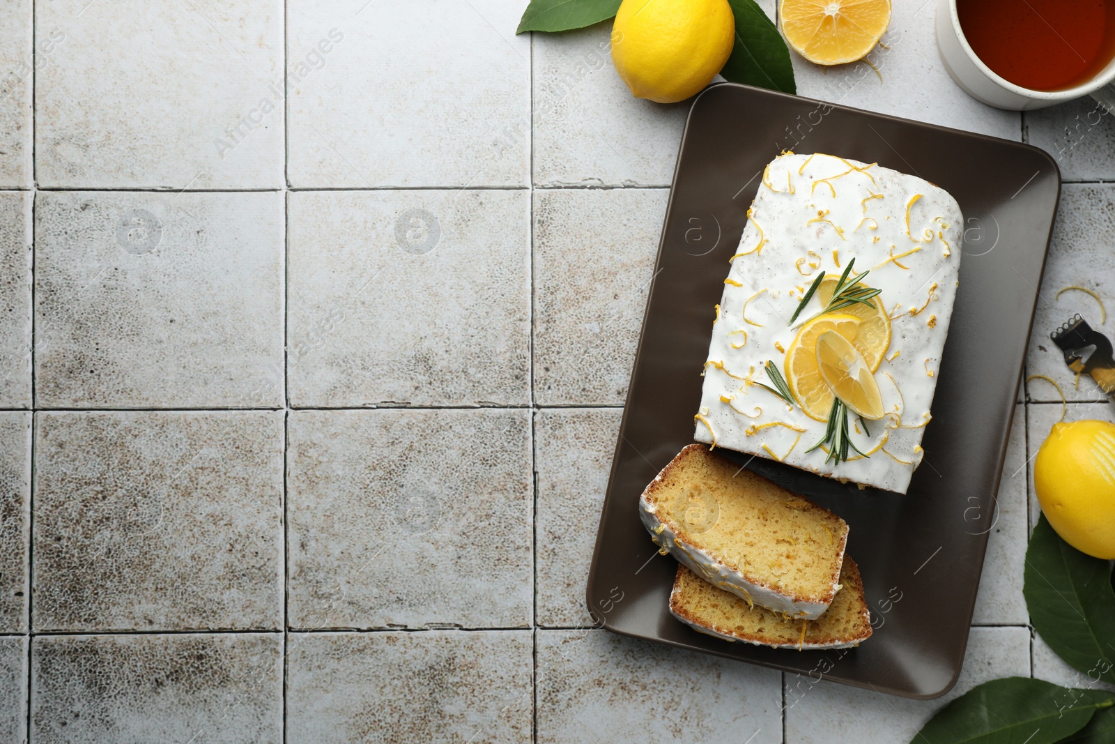 Photo of Tasty lemon cake with glaze, citrus fruits and tea on gray table, flat lay. Space for text