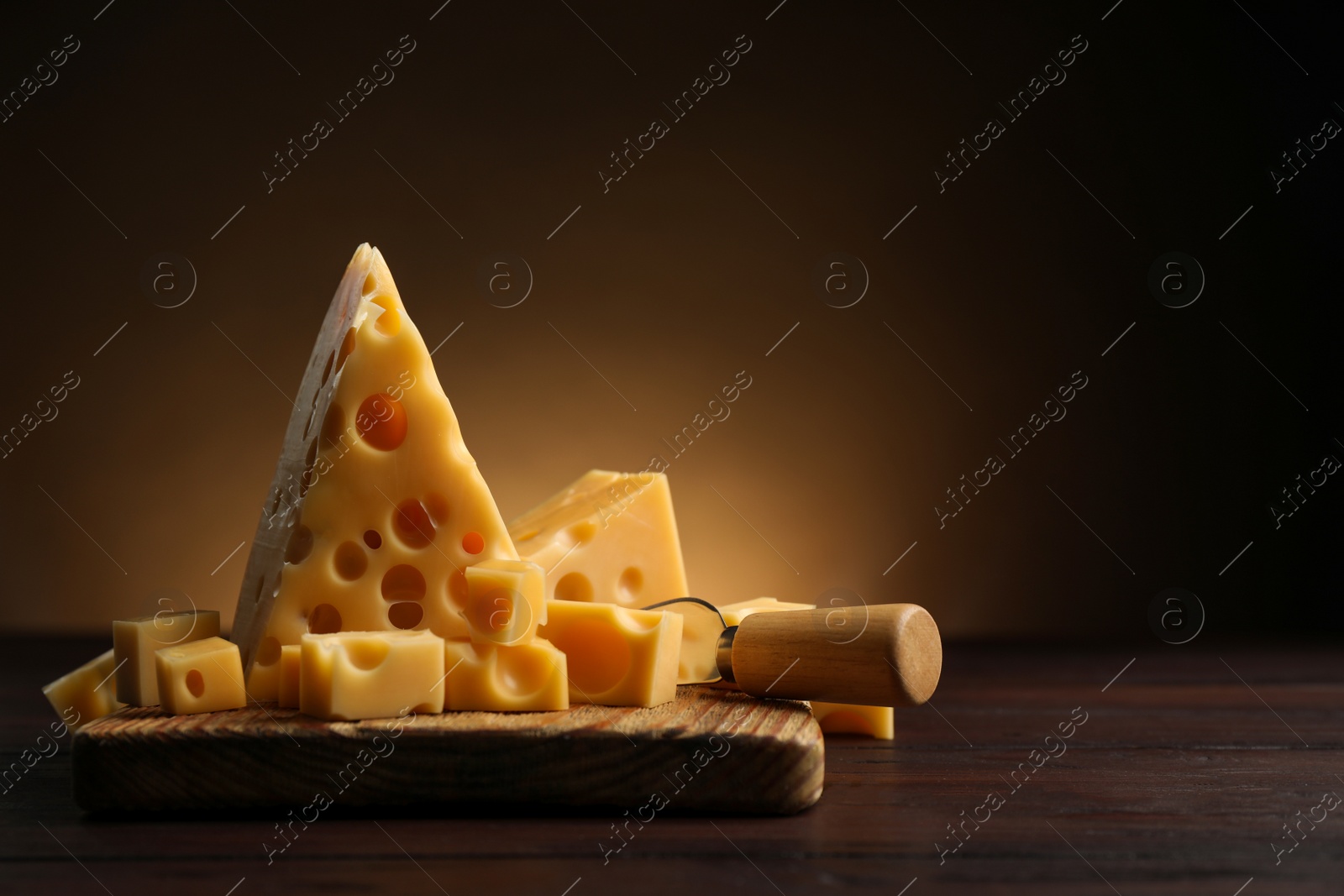 Photo of Pieces of delicious cheese and knife on wooden table. Space for text