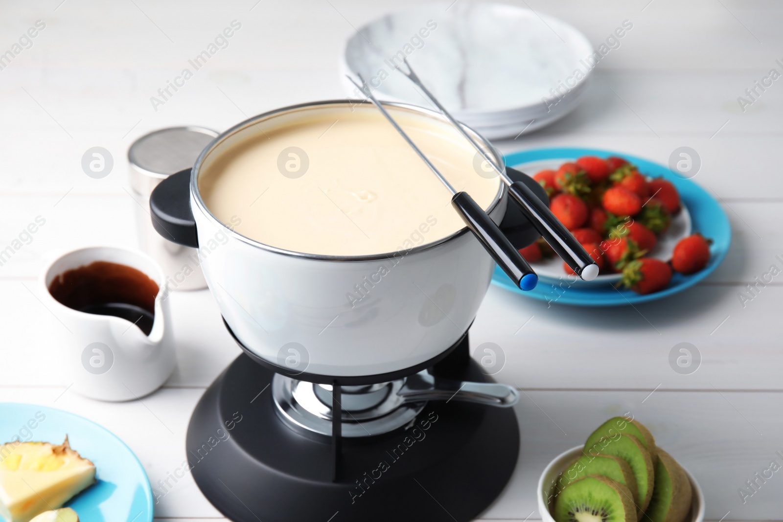 Photo of White chocolate fondue in pot and ripe fruits on wooden table