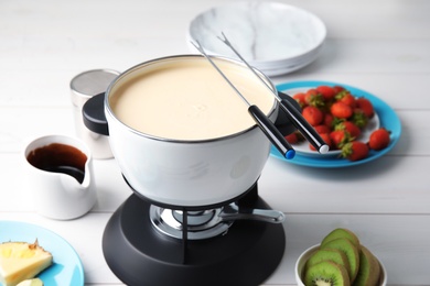 White chocolate fondue in pot and ripe fruits on wooden table