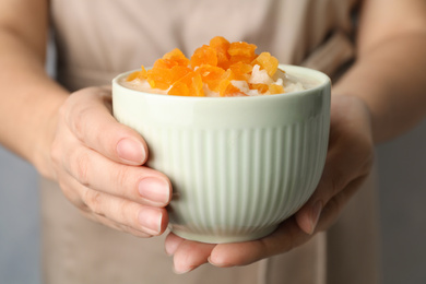 Photo of Woman holding bowl of delicious rice pudding with dried apricots, closeup