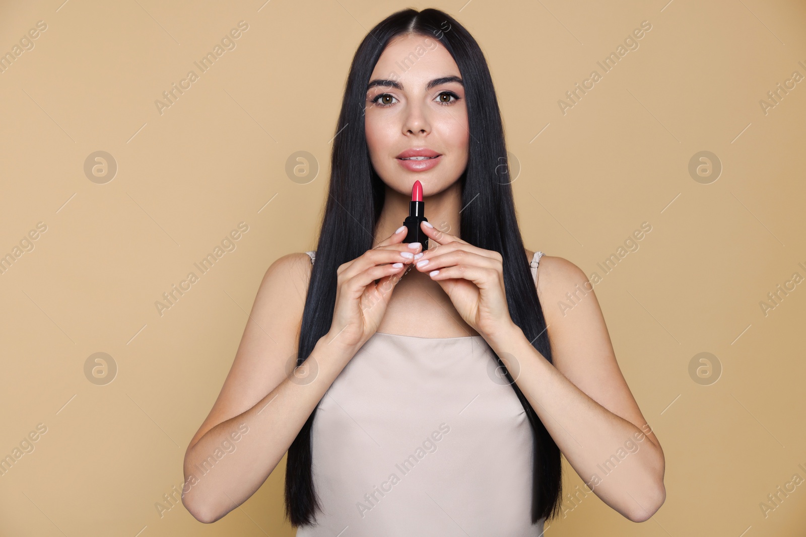 Photo of Young woman with beautiful makeup holding nude lipstick on beige background