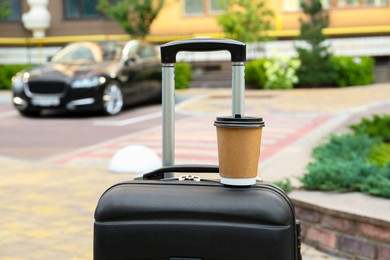 Photo of Paper cup of hot coffee on suitcase outdoors. Takeaway drink