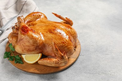 Photo of Tasty roasted chicken with parsley and lemon on light grey table. Space for text