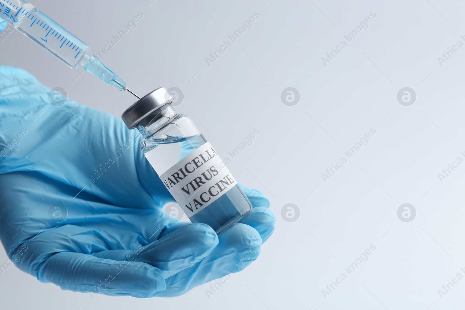 Photo of Closeup view of doctor filling syringe with chickenpox vaccine on light grey background, space for text. Varicella virus prevention