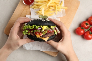 Photo of Woman holding black burger at served table, closeup