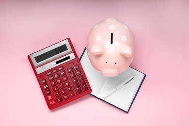 Calculator, piggy bank, pen and notebook on pink background, flat lay