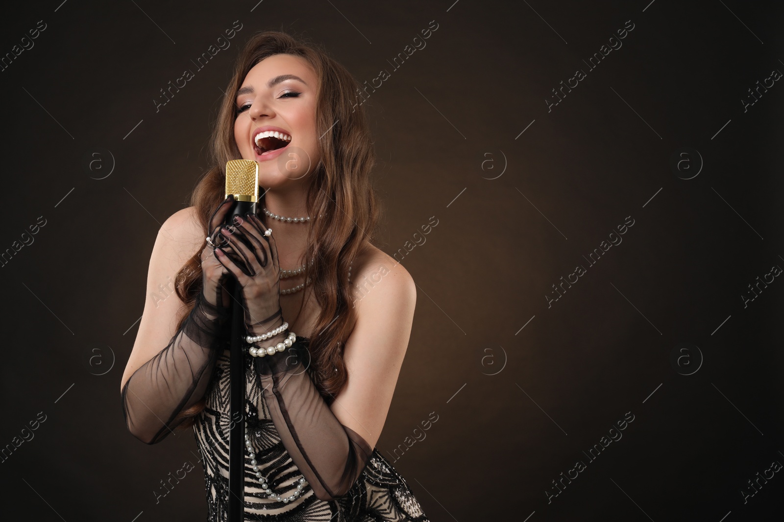 Photo of Beautiful young woman in stylish dress with microphone singing on dark background, space for text