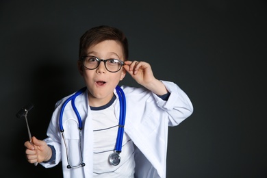 Photo of Cute little child in doctor uniform with reflex hammer on black background