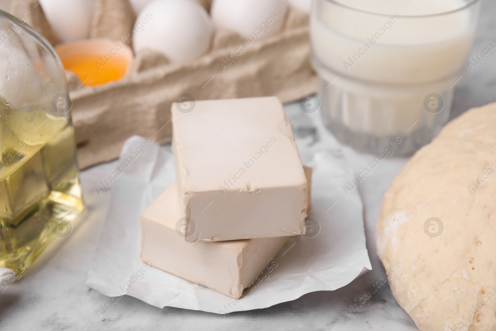 Photo of Blocks of compressed yeast and ingredients on white marble table, closeup