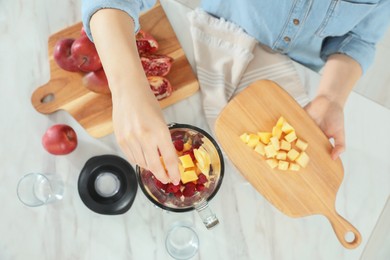 Woman adding mango into blender with ingredients for smoothie at table, top view