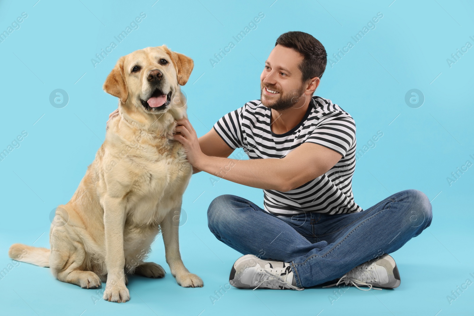 Photo of Man with adorable Labrador Retriever dog on light blue background. Lovely pet