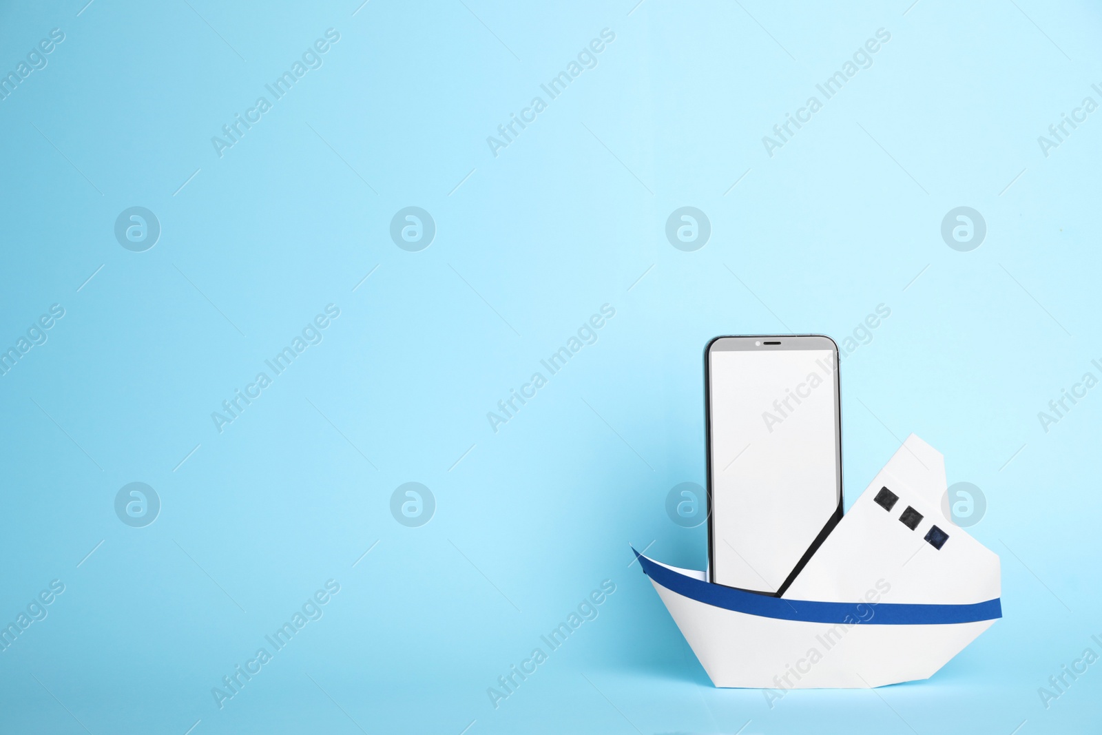 Photo of Modern smartphone in paper boat on light blue background, space for text. Travel concept