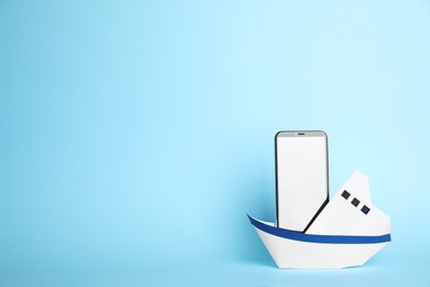 Modern smartphone in paper boat on light blue background, space for text. Travel concept