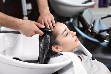 Photo of Stylist washing client's hair at sink in beauty salon