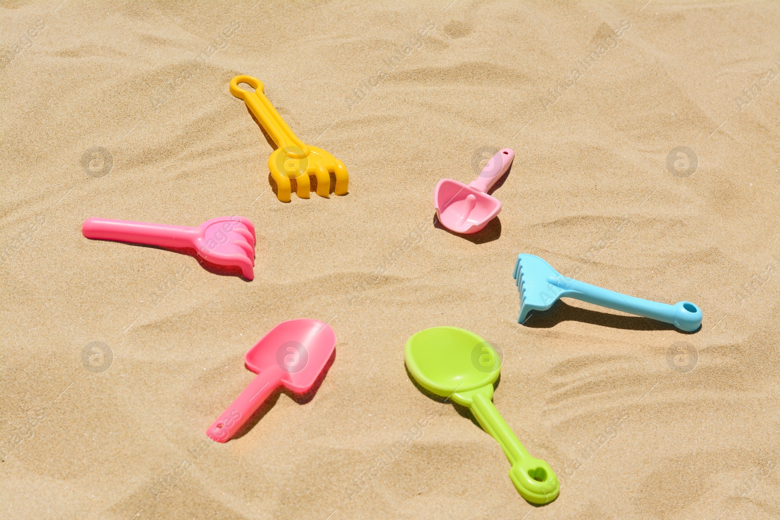 Photo of Bright plastic rakes and shovels on sand. Beach toys