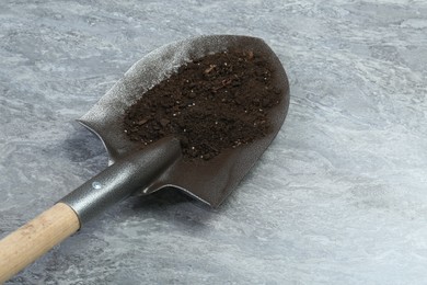 Photo of Metal shovel with fertile soil on gray textured surface, space for text