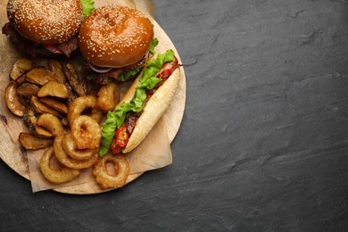 Tasty burgers, hot dog, potato wedges and fried onion rings on black table, top view with space for text. Fast food