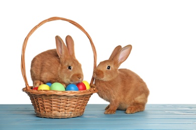 Photo of Cute fluffy bunnies and wicker basket with Easter eggs on light blue wooden table