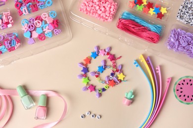 Photo of Handmade jewelry kit for kids. Colorful beads, wristbands, ribbon and bracelets on beige background, flat lay