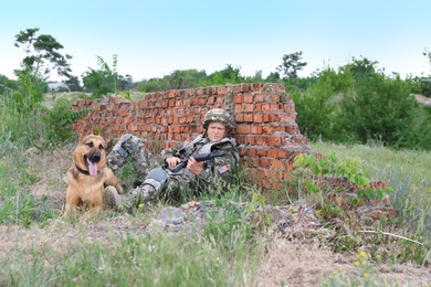 Man in military uniform with German shepherd dog near broken brick wall