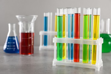 Photo of Test tubes with liquids in stand and flasks on table against light grey background, selective focus