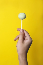 Photo of Woman holding sweet cake pop on yellow background, closeup