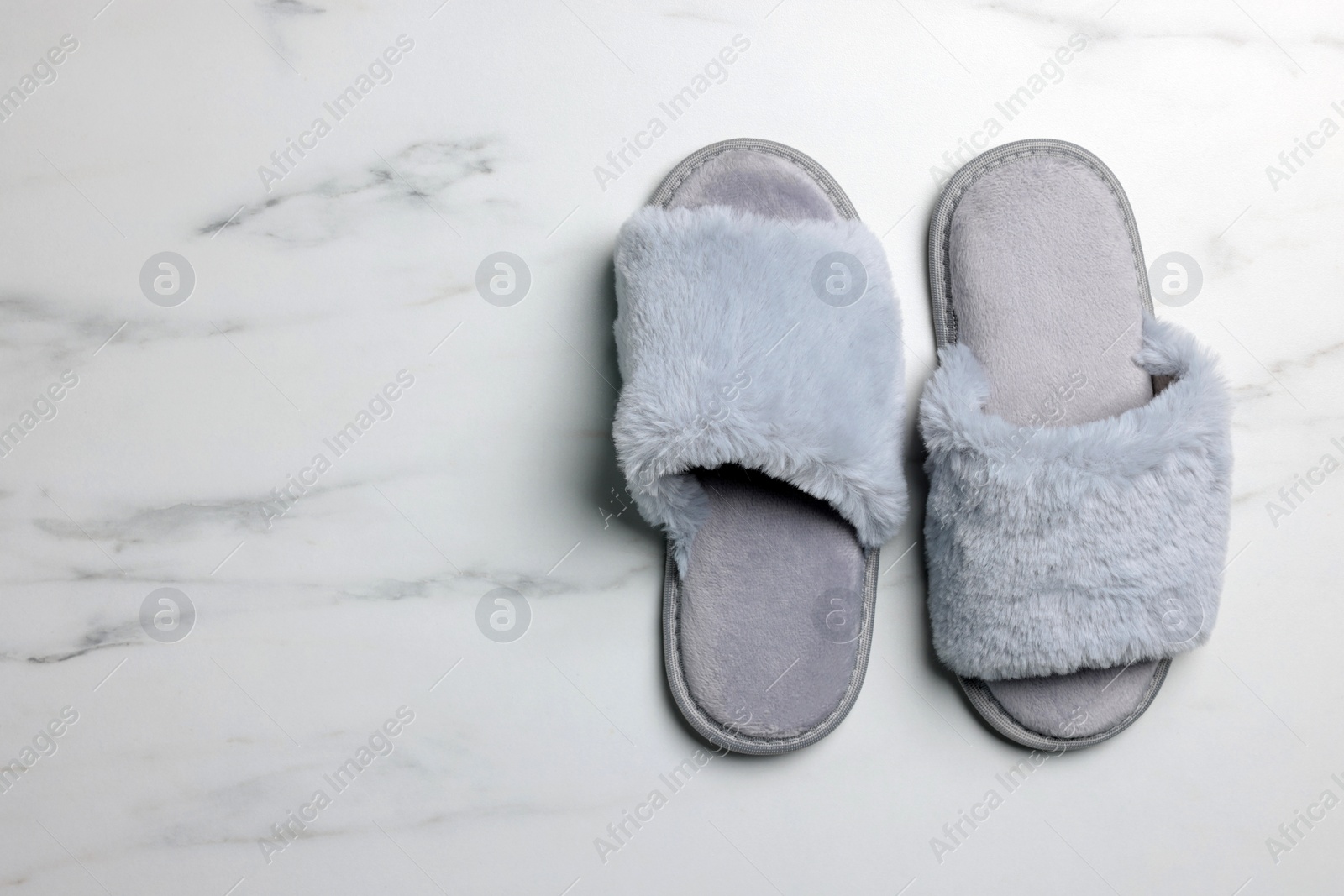 Photo of Pair of soft slippers on white marble floor, top view. Space for text