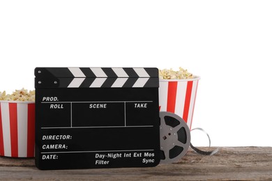 Photo of Movie clapper, buckets of tasty popcorn and film reel on wooden table against white background
