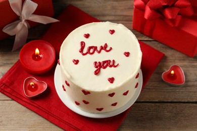 Photo of Bento cake with text Love You, candles and gift boxes on wooden table. St. Valentine's day surprise
