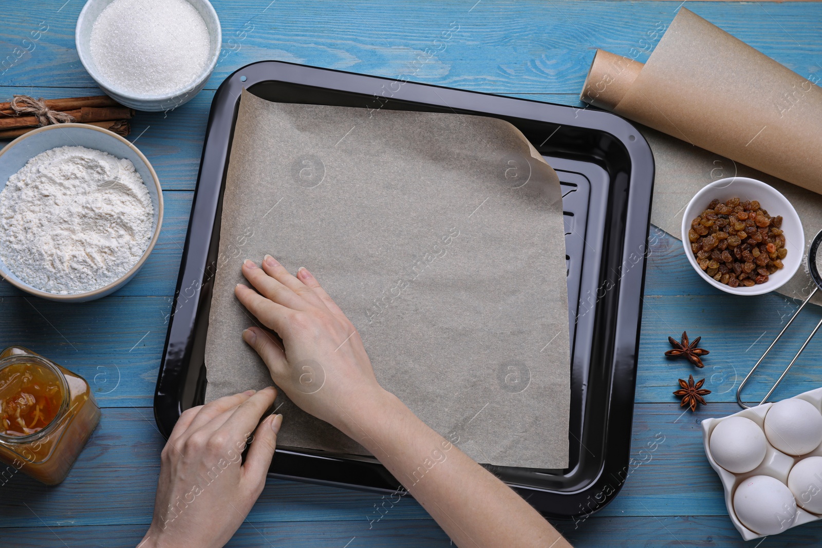 Photo of Woman putting parchment paper into baking pan at light blue wooden table, flat lay